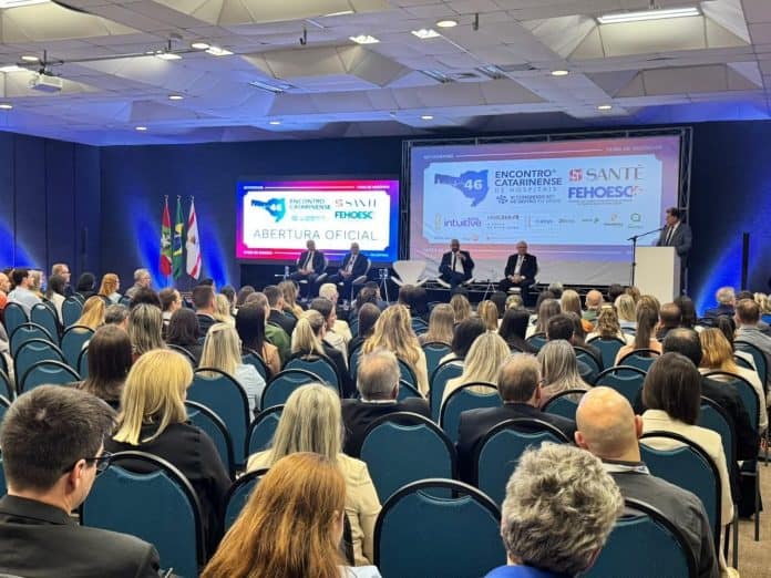 Plateia lotada na abertura oficial do 46º Encontro Catarinense de Hospitais, com autoridades no palco e telões com as marcas FEHOESC e Santé