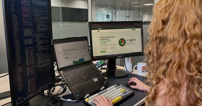 Profissional trabalha diante de monitores que exibem o site da 8ª Conferência Estadual de Ciência, Tecnologia e Inovação de Santa Catarina, em escritório da SCTI