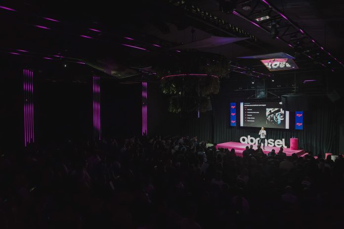 Palestrante no palco do Abrasel Summit 2026, em Florianópolis, diante de plateia lotada, com o logo da Abrasel e telão ao fundo
