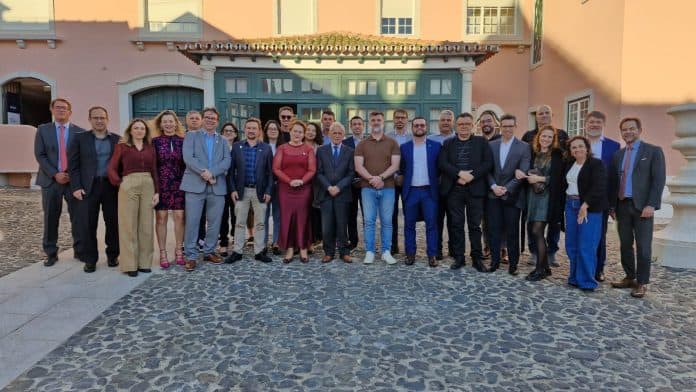 Grupo de cerca de 30 integrantes da missão catarinense de cidades inteligentes posando lado a lado em um pátio de pedras diante de um prédio histórico rosado com porta verde