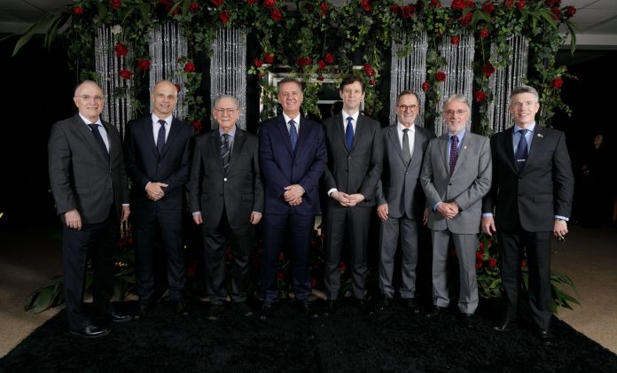 Oito médicos de terno posam lado a lado diante de um painel de rosas vermelhas no Baile do Médico da ACM, em Florianópolis