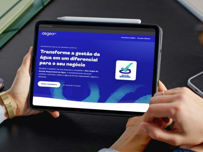 Mãos seguram um tablet com a página do recadastramento de grandes clientes da Aegea