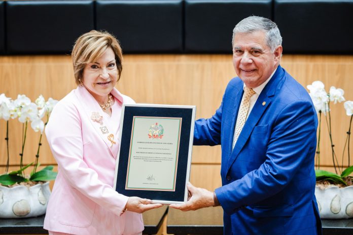 Integrante da Rede Feminina de Combate ao Câncer, de blazer rosa, recebe placa comemorativa dos 40 anos durante sessão na Assembleia Legislativa de Santa Catarina