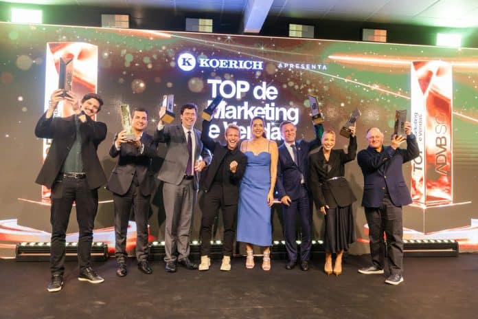 Vencedores do Prêmio Top de Marketing e Vendas 2026 da ADVB/SC erguem troféus no palco, diante de telão com a marca Koerich e o título TOP de Marketing e Vendas