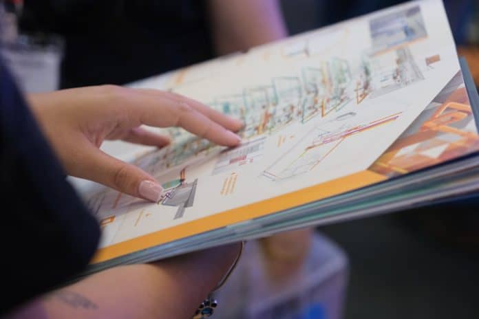 Mão de uma pessoa folheando um catálogo impresso com desenhos técnicos de projeto de instalações em 3D