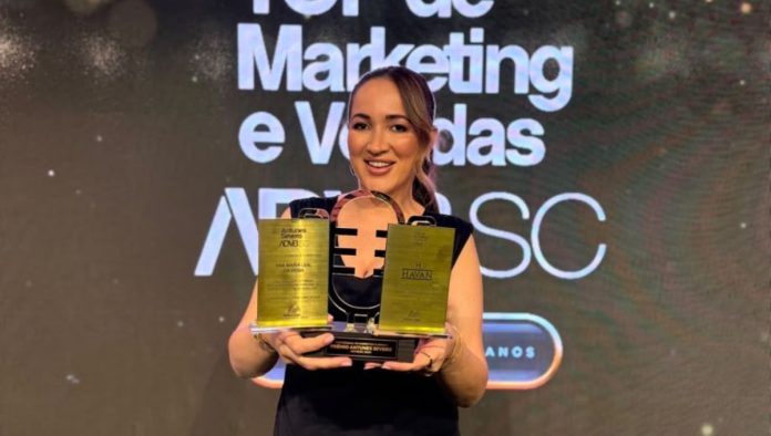 Ana Maria Leal da Veiga, gerente de Marketing da Havan, sorri segurando os troféus do Prêmio Antunes Severo 2026 em frente ao painel do Top de Marketing e Vendas da ADVB/SC
