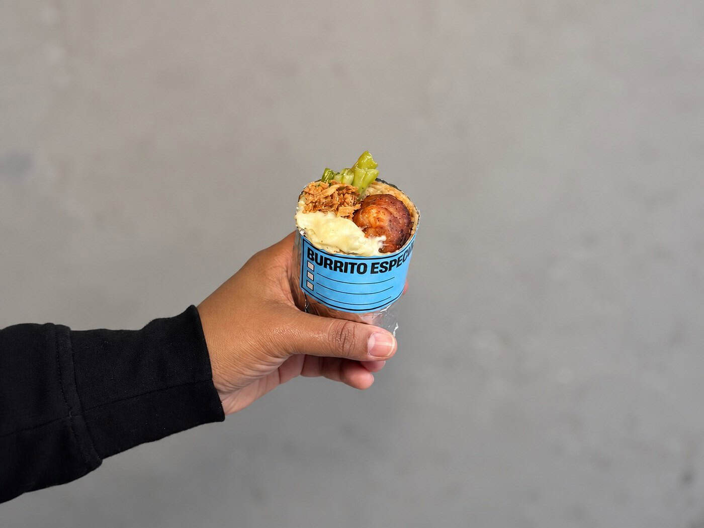 Mão segura o burrito Napoleon embrulhado em papel, com o recheio à mostra