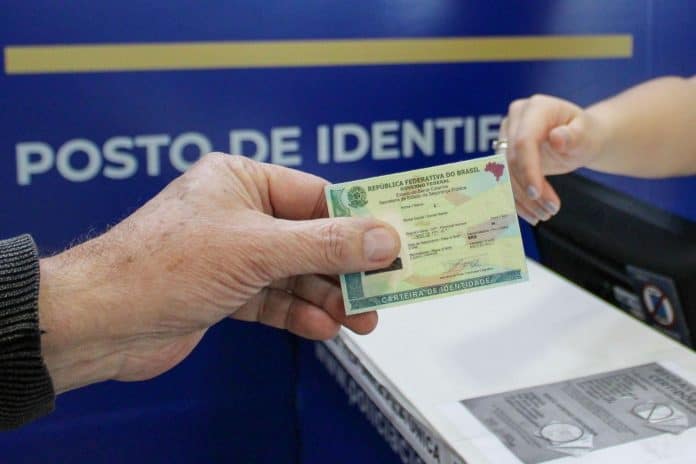Mão entrega Carteira de Identidade Nacional em posto de identificação da Polícia Científica de Santa Catarina
