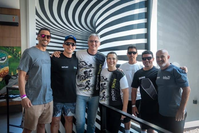 Grupo de sete pessoas posa na Casa Irada, em Jurerê Internacional, com o ex-jogador de vôlei Paulão ao centro, durante o IRONMAN 70.3 Florianópolis