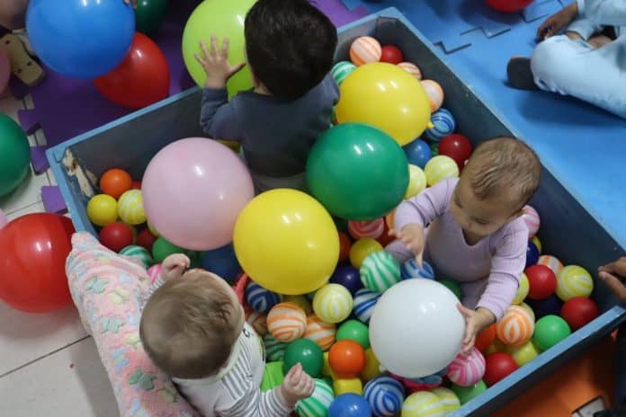 Bebês brincam em uma piscina de bolinhas e balões coloridos