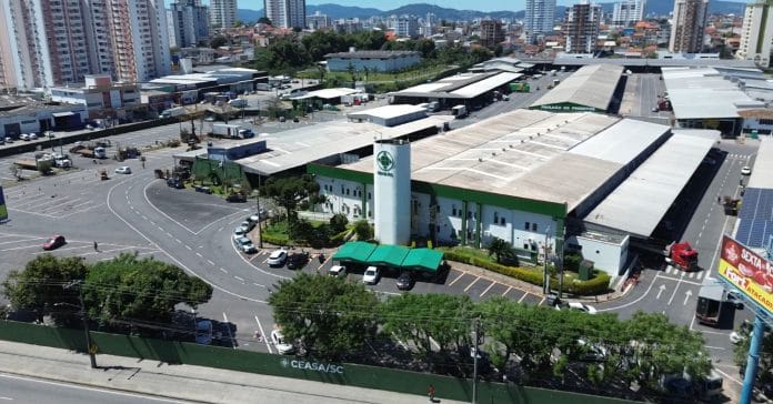 Vista aérea da Ceasa/SC, com pavilhões de comercialização, torre de caixa-d'água com o logotipo da central e pátio de estacionamento