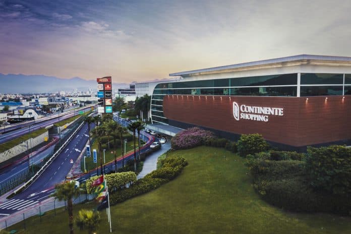 Fachada do Continente Shopping ao entardecer, com a BR-101 à esquerda e o letreiro do shopping na parede de revestimento escuro
