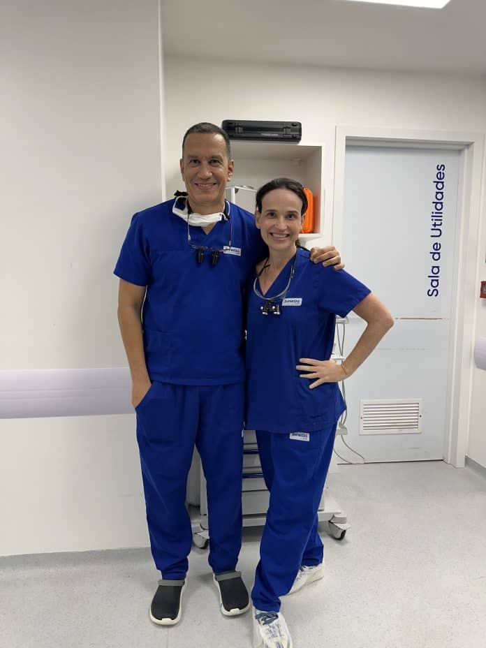 Os médicos Otávio Boaventura, cirurgião plástico, e Débora Cadore, dermatologista, posam lado a lado com roupa cirúrgica azul