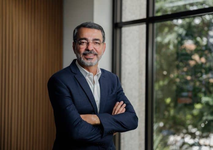 O empresário Paulo Zahr, de terno azul e braços cruzados, ao lado de uma janela