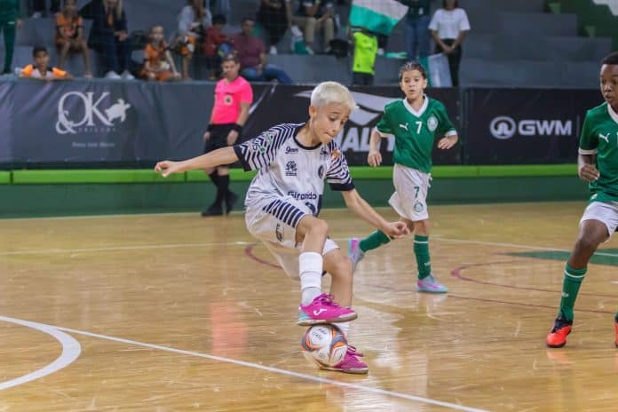 Matheus Stefanski, de cabelo descolorido e uniforme listrado da APAFF, conduz a bola em quadra de futsal