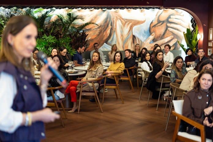 Esther Schattan, de colete escuro e microfone na mão, fala a convidados sentados no restaurante da CASACOR SC