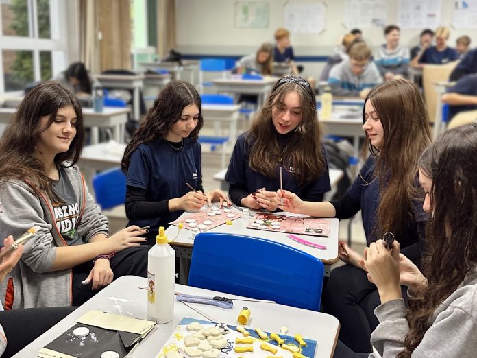 Estudantes adolescentes trabalham em grupo em mesas de sala de aula com materiais de artesanato