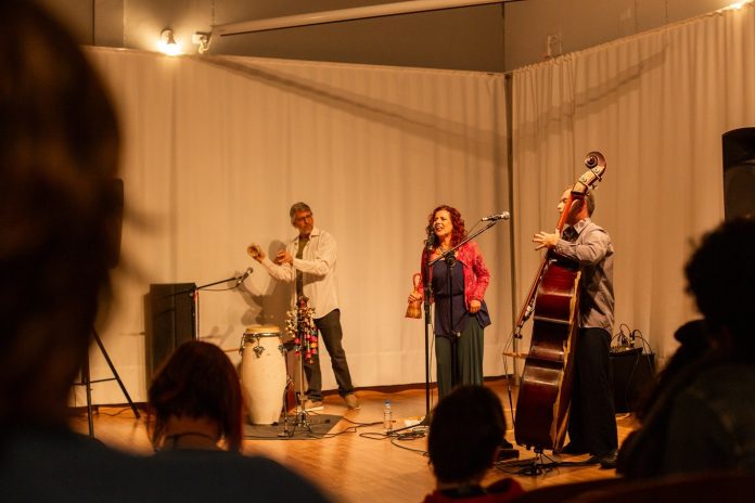 Fernanda Rosa canta ao centro do palco, ao lado do contrabaixista Mateus Costa e do percussionista Rodrigo Gudin Paiva, diante da plateia