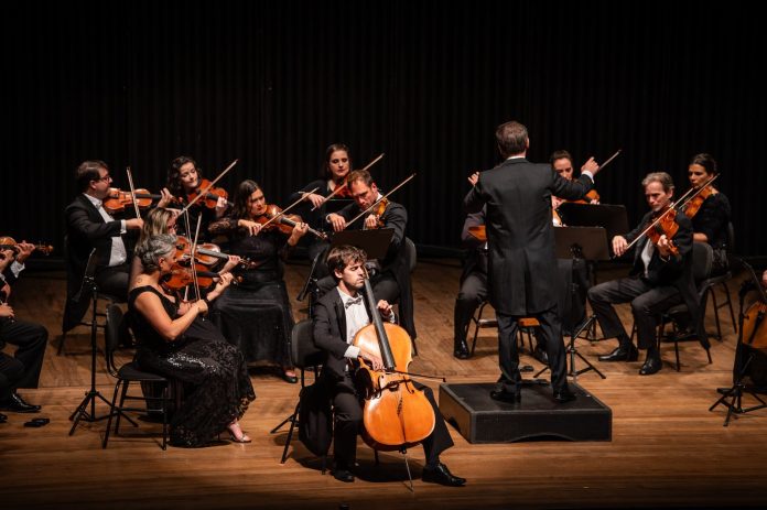 Camerata Florianópolis em concerto no palco, com violoncelista em destaque à frente da orquestra