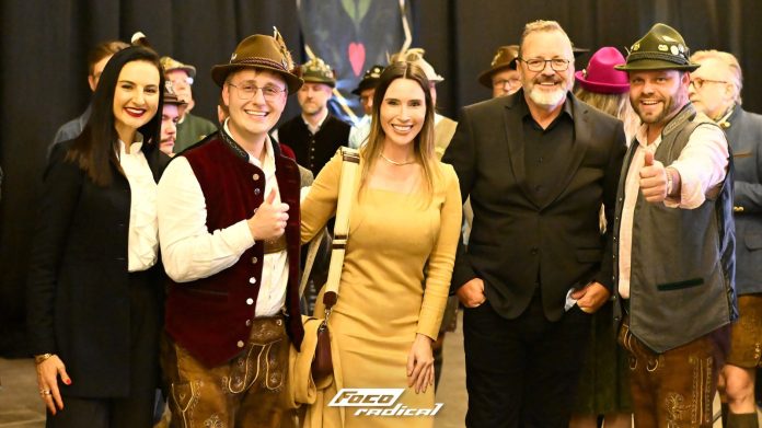 Visitantes com trajes típicos germânicos, chapéus tiroleses e coletes sorriem e fazem sinal de positivo para a câmera
