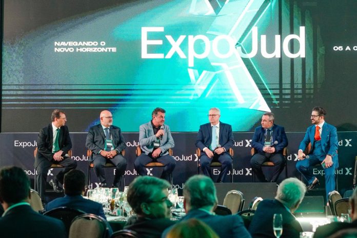 Seis participantes sentados no palco de um talk show da ExpoJud, em Brasília, diante de telão com a frase Navegando o novo horizonte