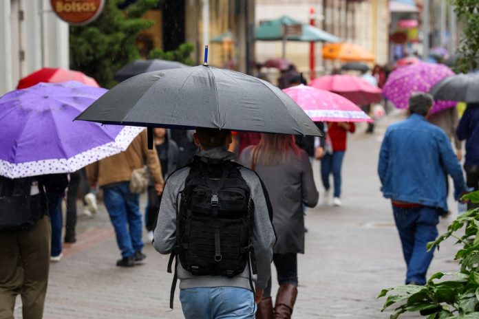 Pedestres com guarda-chuvas caminham por calçadão em dia de chuva, em imagem ilustrativa