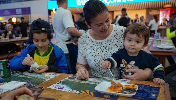 Mãe com dois filhos comendo ostras gratinadas em mesa da praça de alimentação da Fenaostra, no CentroSul, em Florianópolis
