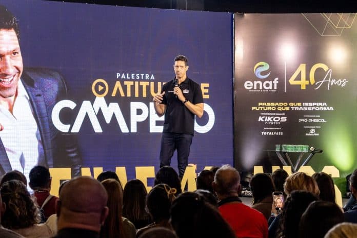 Gustavo Borges no palco do ENAF, de camisa preta e microfone na mão, diante da plateia