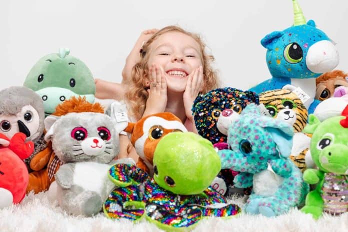 Menina sorridente abraçada a vários bichos de pelúcia coloridos