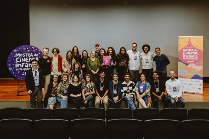 Cerca de 30 participantes do Encontro Nacional de Cinema Infantil posam em grupo no palco, ao lado de banners da Mostra de Cinema Infantil de Florianópolis