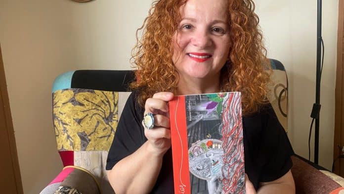 A escritora Rosane Cordeiro sorri segurando um exemplar do livro Fios
