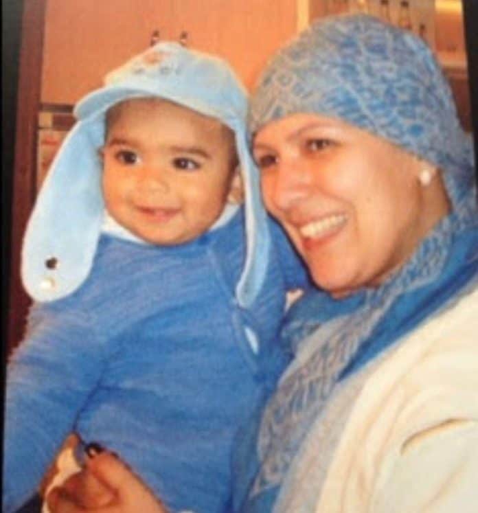 Gisele Toledo, de lenço azul na cabeça durante o tratamento contra o câncer de mama, sorri com o filho bebê no colo