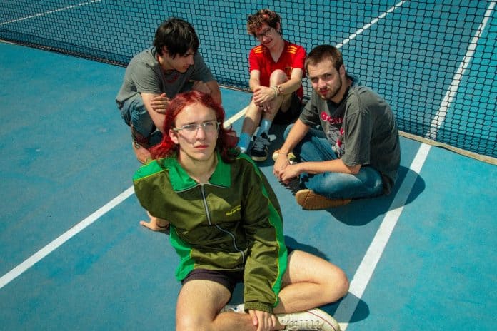 Integrantes da banda Chococorn and The Sugarcanes sentados em uma quadra de tênis azul
