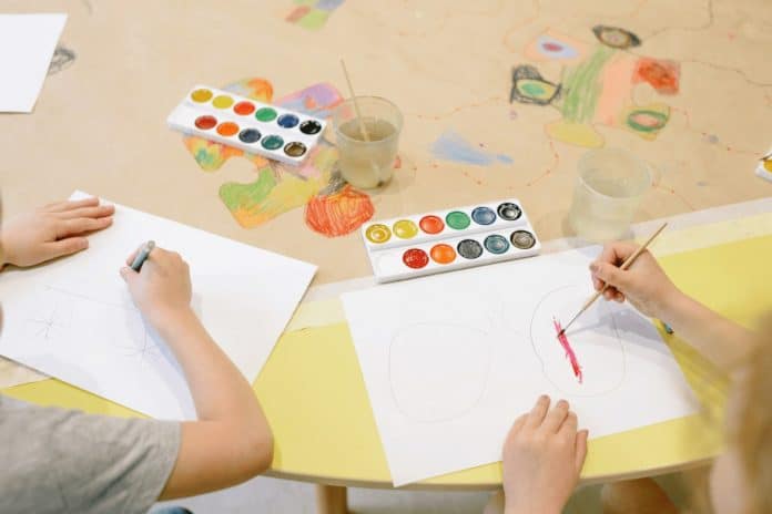 Crianças pintam desenhos com aquarela em uma mesa de oficina
