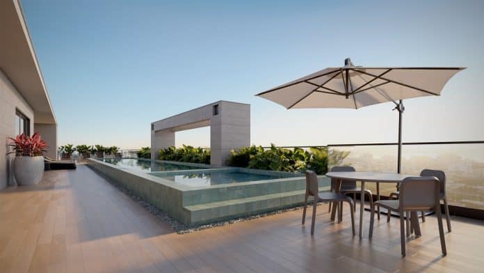 Perspectiva de área de lazer na cobertura com piscina, mesa e guarda-sol em empreendimento da Cota Empreendimentos