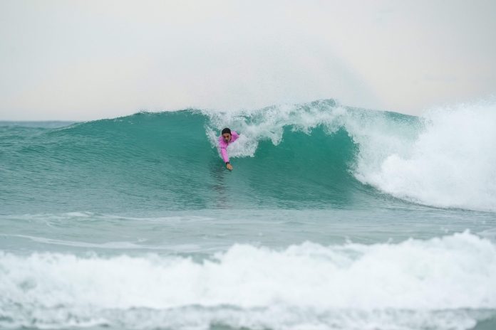 Atleta de bodysurf com lycra rosa desliza dentro de uma onda verde-azulada