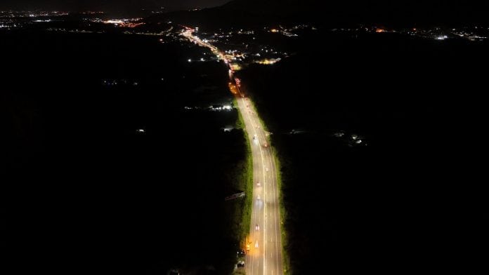 Vista aérea noturna de rodovia iluminada com LED cortando área escura na Grande Florianópolis