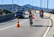 Guia do fim de semana em Floripa: 12 planos para 17 e 18 de outubro de 2026 Atleta de ciclismo do IRONMAN 70.3 Florianópolis pedalando em pista compartilhada com carros
