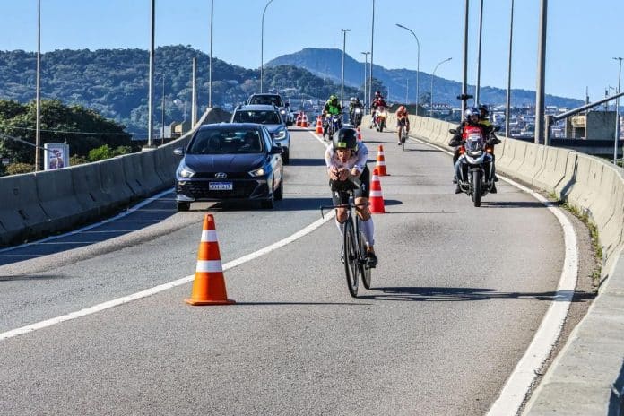 Atleta de ciclismo do IRONMAN 70.3 Florianópolis pedalando em pista compartilhada com carros