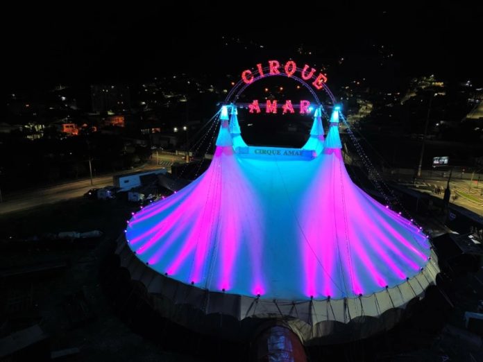 Lona do Cirque Amar iluminada em rosa e azul à noite na Via Expressa Sul, em Florianópolis