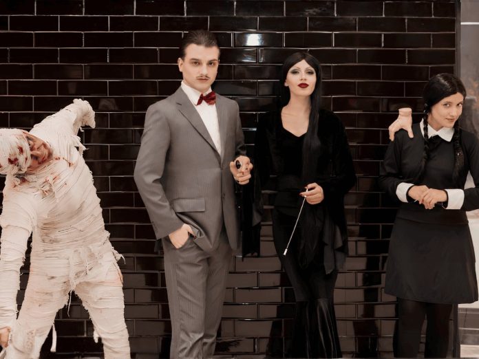 Personagens da Família Addams e uma múmia posam em frente a parede de tijolos pretos no Villa Romana Shopping