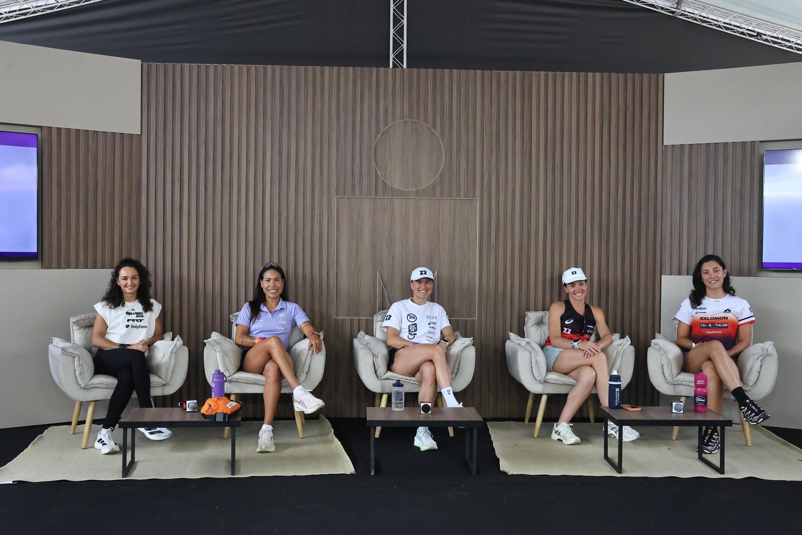 Cinco triatletas sentadas em poltronas, lado a lado, no palco da coletiva de imprensa do IRONMAN 70.3 Florianópolis