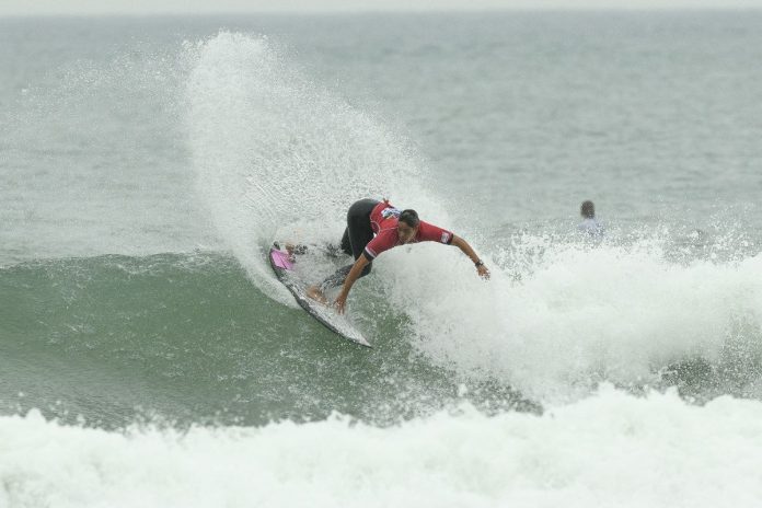 Surfista Michel Demétrio, de lycra vermelha, faz manobra e levanta spray em onda na praia da Joaquina