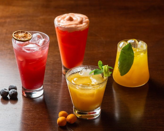Quatro mocktails coloridos do Restaurante Raízes sobre mesa de madeira