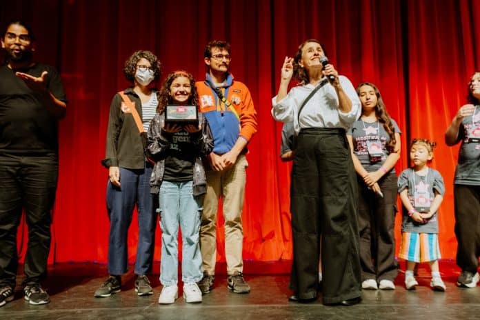 Equipe da Mostra e crianças do júri no palco do CIC, diante de cortina vermelha, durante a premiação da 25ª Mostra de Cinema Infantil de Florianópolis