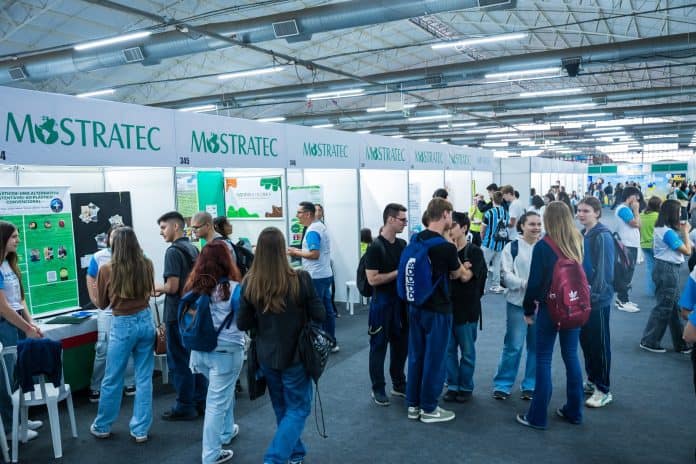 Estudantes circulam entre estandes de projetos científicos com painéis da Mostratec em um pavilhão de feira