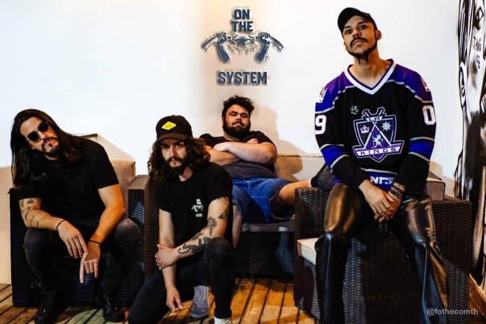 Integrantes da banda On The System, tributo ao System of a Down, posam sentados em sofás diante de parede branca com o logo da banda