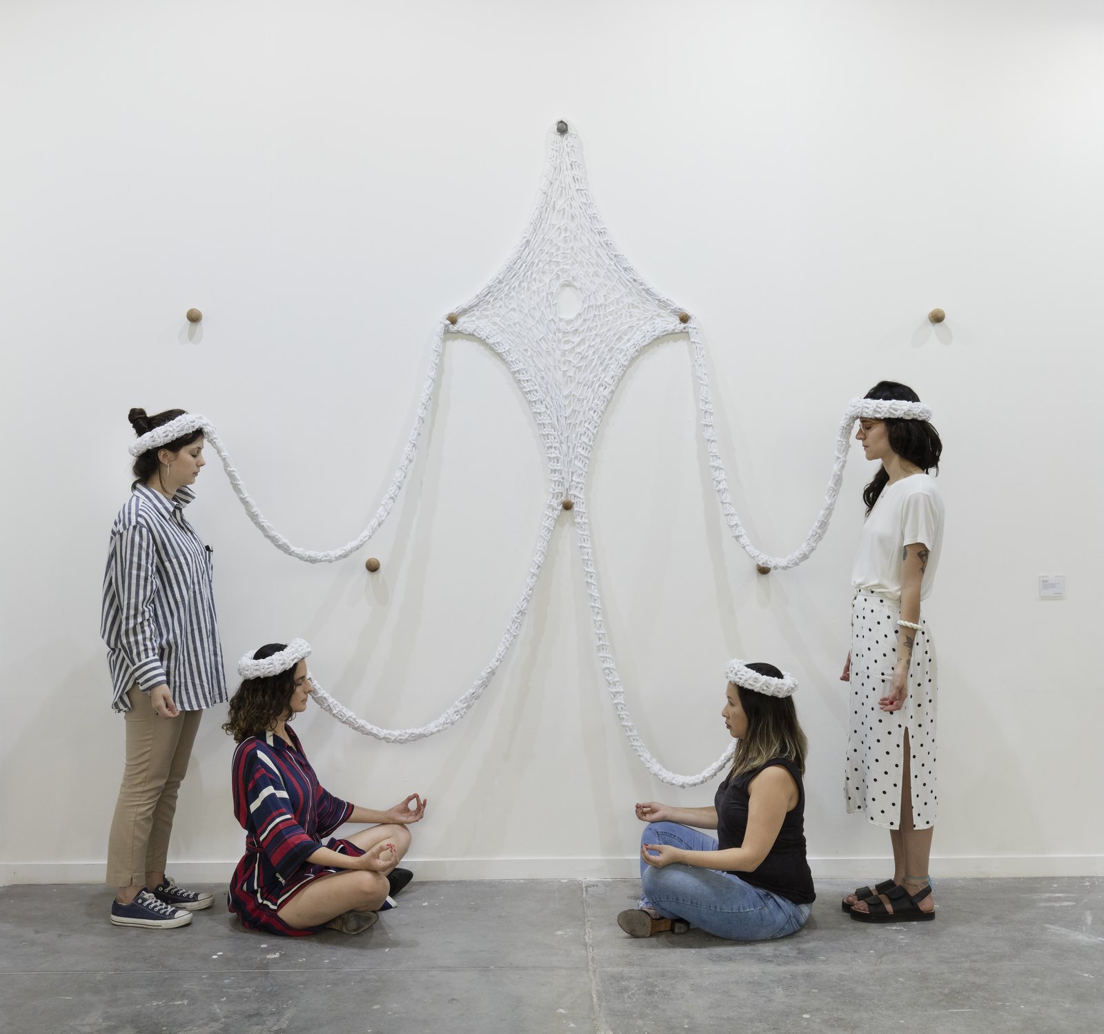 Visitantes interagem com a obra Oxalá, de Ernesto Neto, peça em crochê branco presa à parede de uma galeria