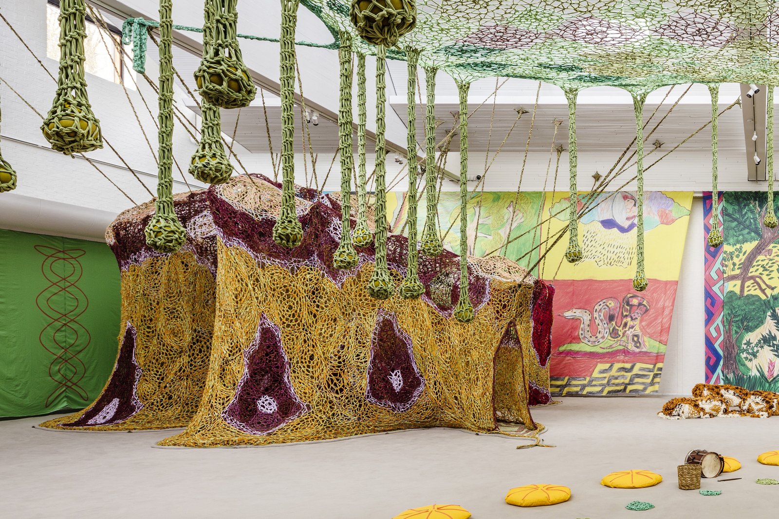 Instalação Womboa, de Ernesto Neto, com estruturas em crochê amarelo e roxo e elementos suspensos em um salão expositivo
