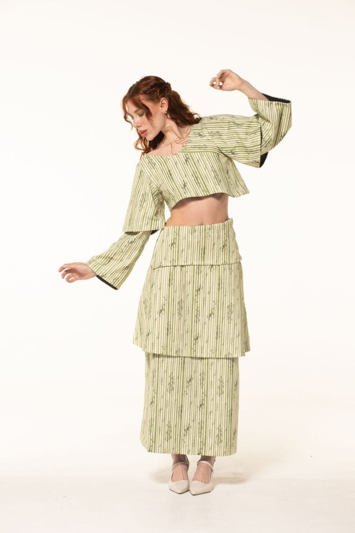 Modelo com conjunto de saia longa e blusa de mangas amplas em tecido verde-claro texturizado posa em fundo branco